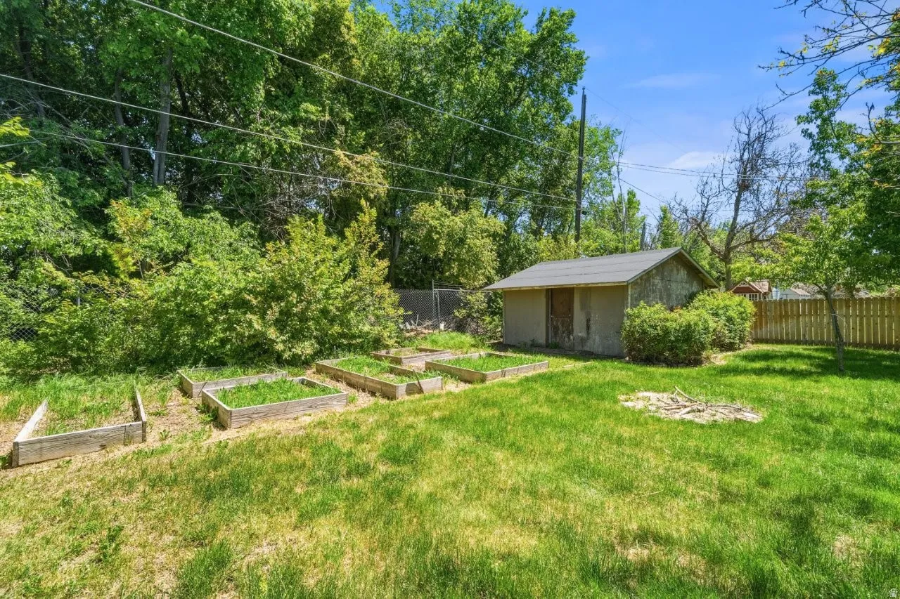Backyard features multiple raised garden beds ready for planting, a storage shed, and mature trees providing natural shade and privacy. Gardeners and outdoor enthusiasts will love the potential here.