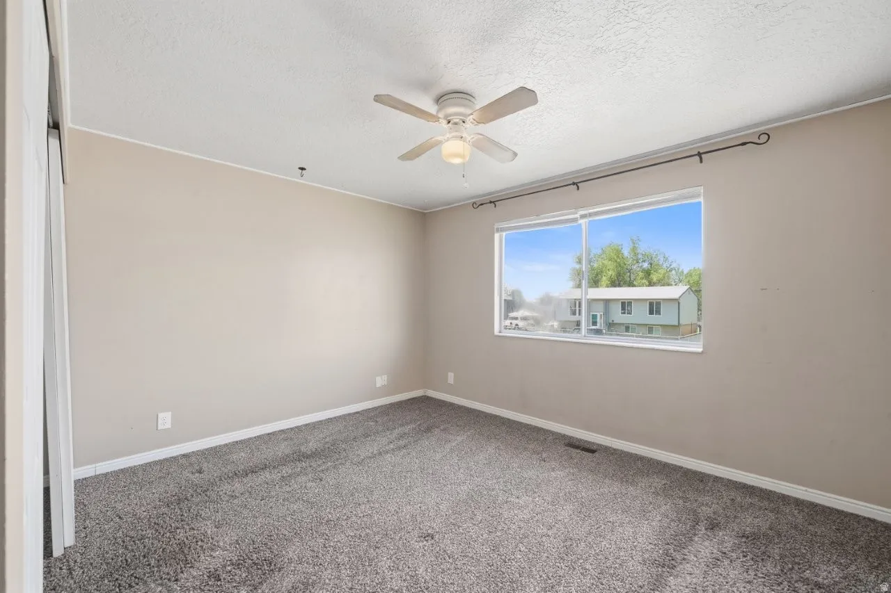 Comfortable bedroom featuring a double sliding door closet, ceiling fan, carpet, and a window with natural light. Conveniently located just off the hall with easy kitchen access.