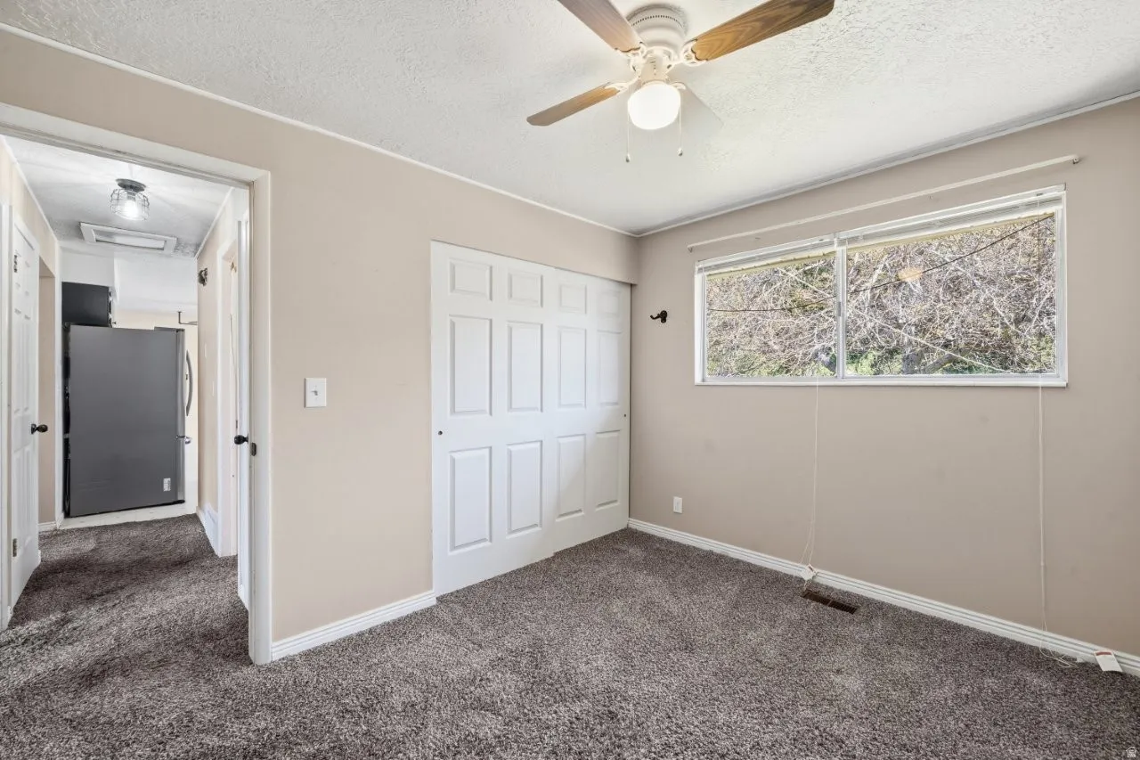 Comfortable bedroom featuring a double sliding door closet, ceiling fan, carpet, and a window with natural light. Conveniently located just off the hall with easy kitchen access.