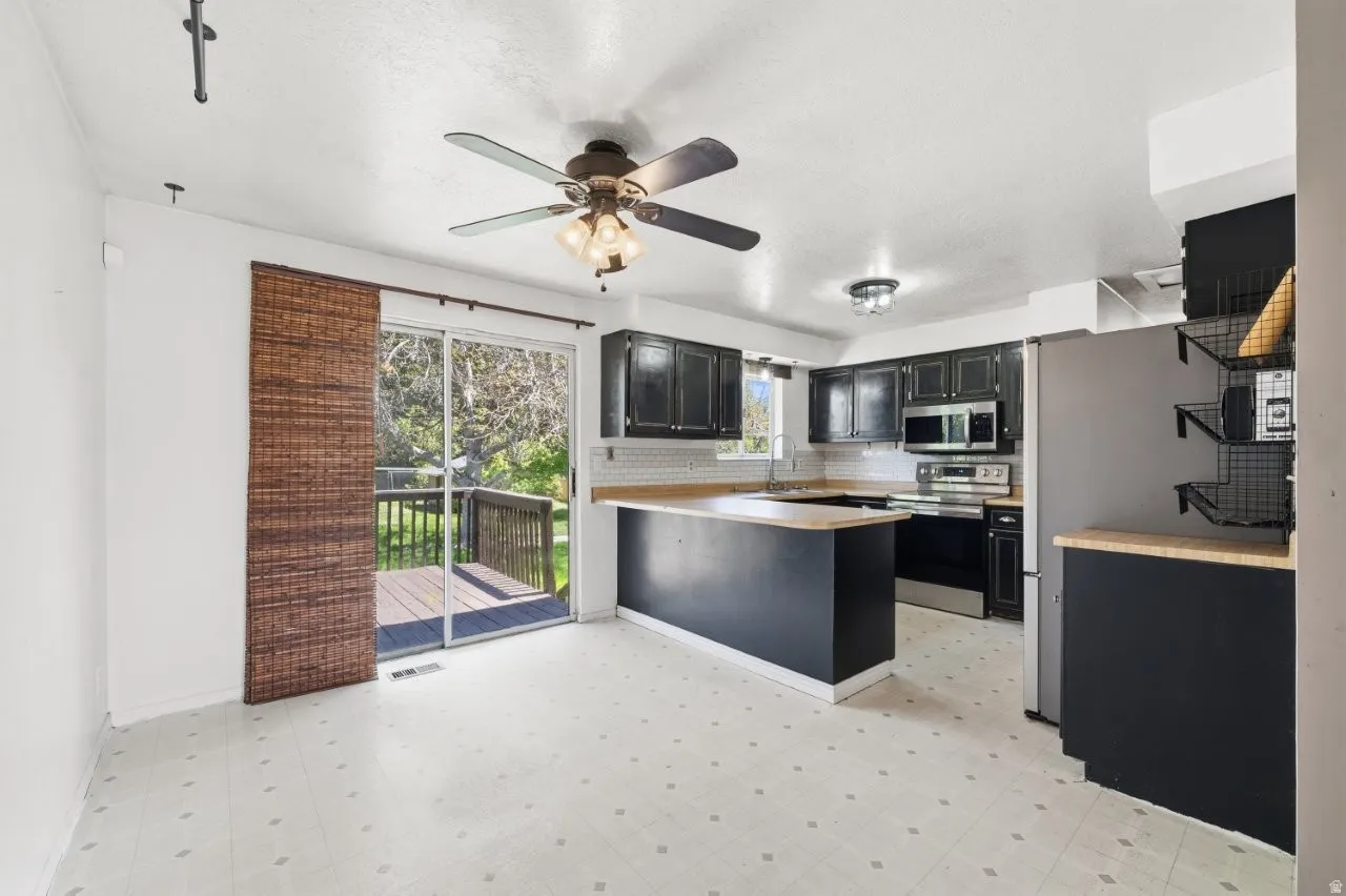Functional kitchen features dark distressed cabinetry, butcher block countertops, subway tile backsplash, stainless steel appliances, and a peninsula with seating potential. Sliding glass door opens directly to the back deck, making indoor/outdoor enterta