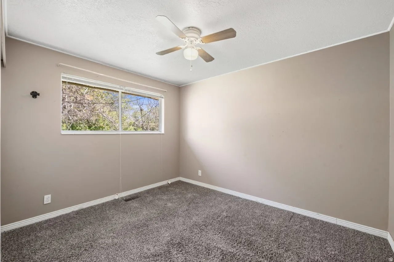 Good-sized bedroom with carpet, ceiling fan, and a window overlooking mature trees. Neutral tones make it move-in ready or a fresh canvas for your own style.