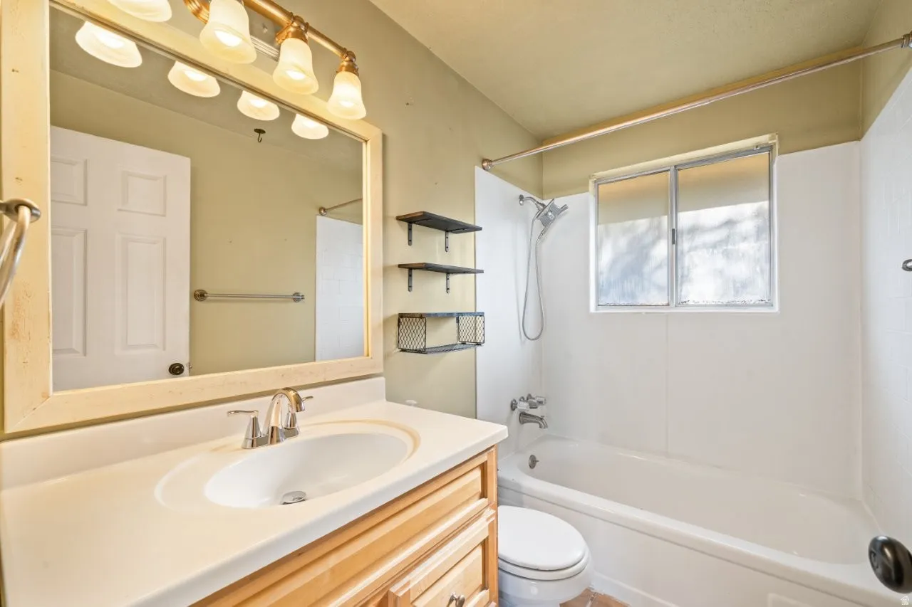Bathroom featuring a light wood-finish vanity with an integrated sink, a rectangular framed mirror, and a five-light vanity fixture
