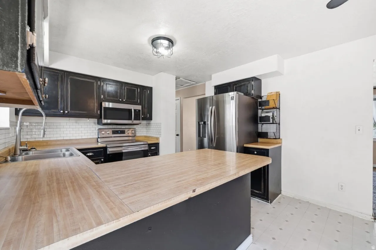 Generous counter space anchors this kitchen, with distressed dark cabinetry, subway tile backsplash, stainless steel appliances, and an industrial-style ceiling fixture. Plenty of prep and storage space for the buyer ready to put their personal stamp on i