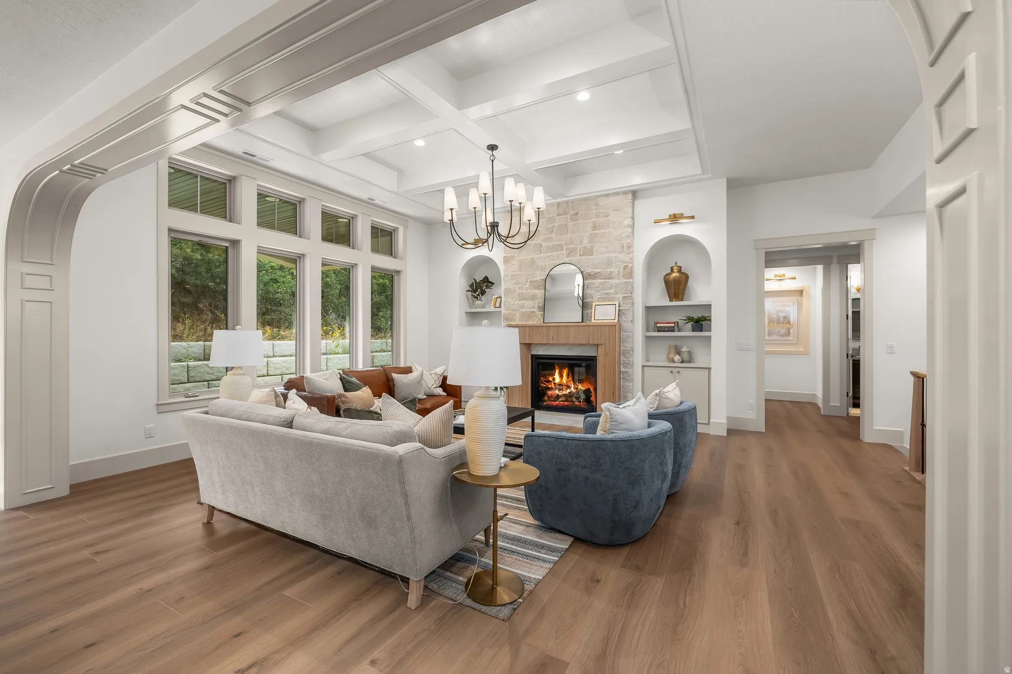 Living area featuring wood-finish flooring, a coffered ceiling, a stone-faced fireplace with a wood mantel, and built-in arched shelving