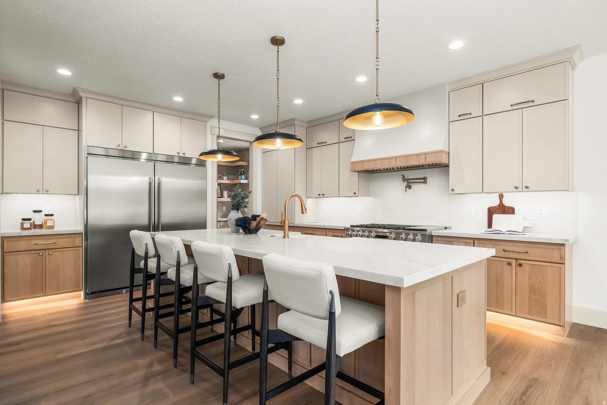 Kitchen featuring wood-finish flooring, a large central island with seating, stainless steel appliances, and a custom range hood