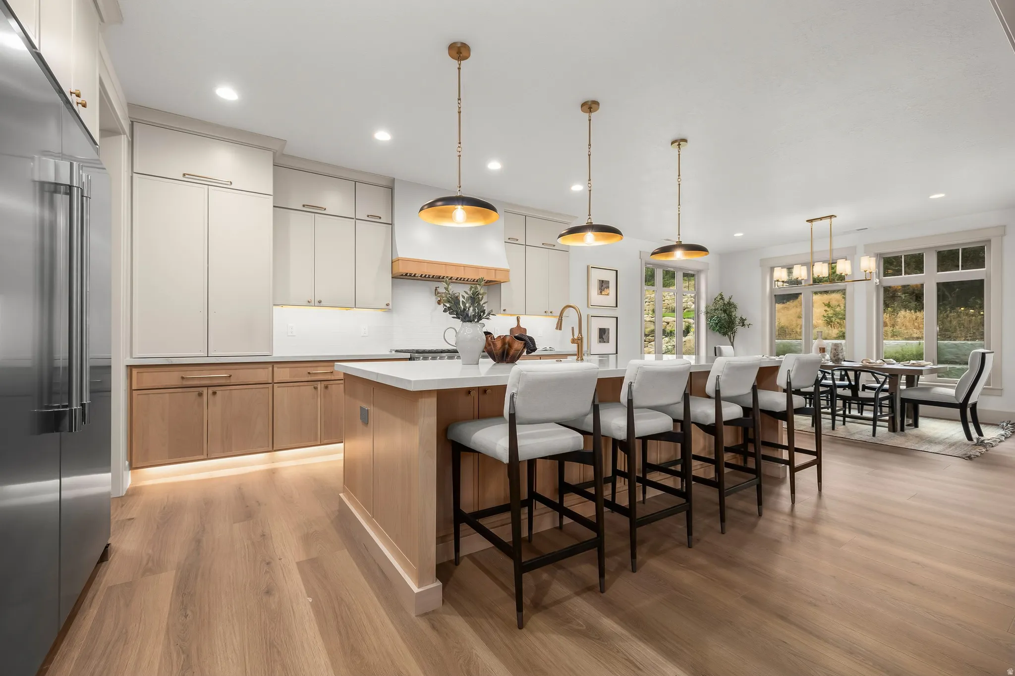 Stainless steel refrigerator and appliances, recessed lighting, wood-finish flooring, kitchen island with seating, and a dining area with expansive windows