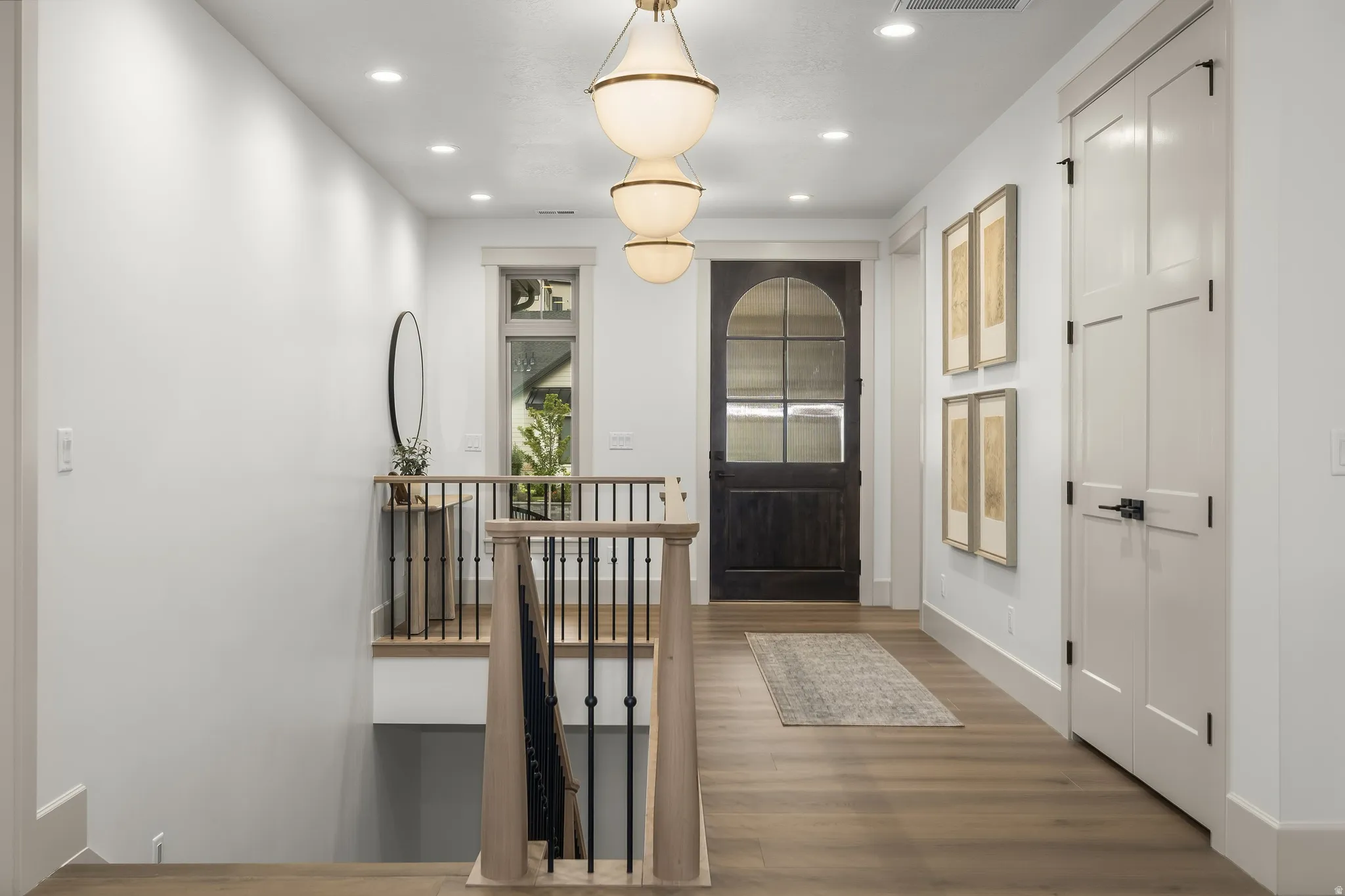 Hardwood-finish flooring, recessed lighting, multi-panel doors with matte black hardware, custom arched entry door, and a multi-tiered chandelier