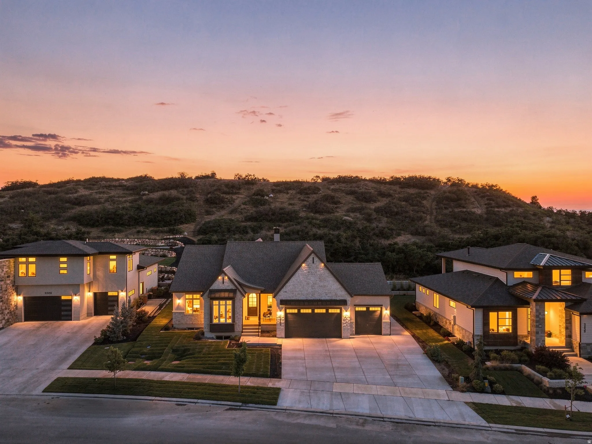 Modern architectural design featuring stone and stucco exterior finishes, gabled rooflines, multiple attached garages, and concrete driveways