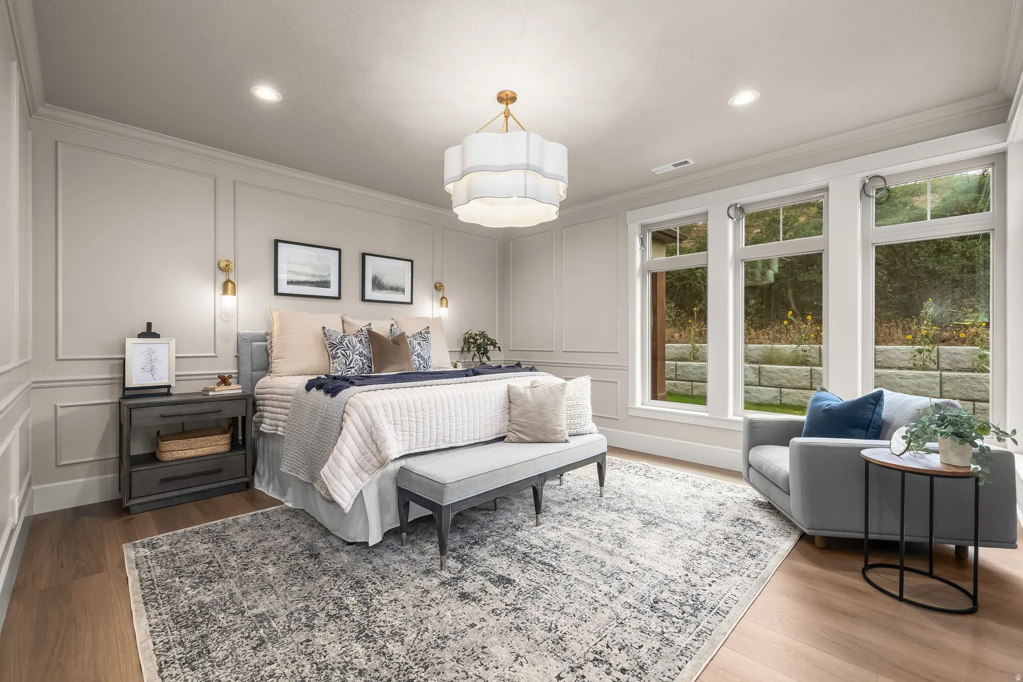 Wood-finish flooring, a wall with decorative molding, and a central tiered chandelier