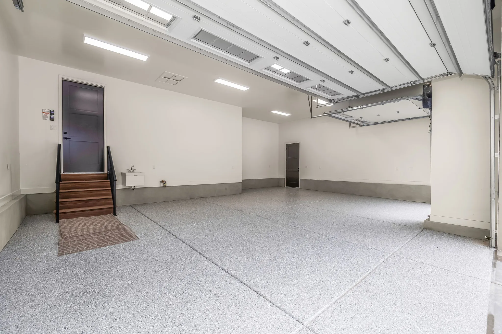 Spacious garage featuring a light-colored epoxy floor coating, white walls, and bright overhead lighting