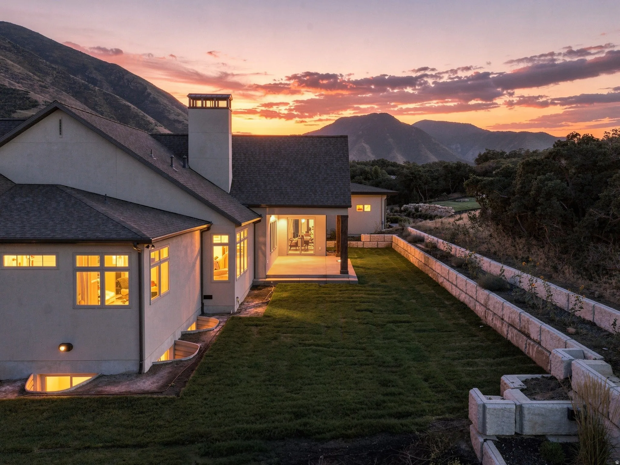Stucco exterior with a shingle roof, featuring a covered patio, terraced landscaping, and a manicured lawn