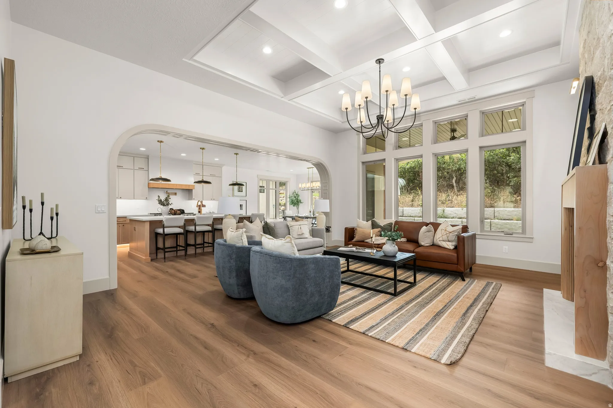 Wood-finish flooring, coffered ceiling, large picture windows, arched entryway, and a stone-clad fireplace