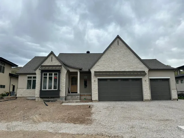 View of front facade featuring a standing seam roof, covered porch, stone siding, a shingled roof, and gravel driveway