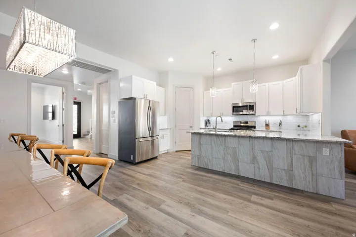 Open-concept kitchen and dining area featuring wood-finish flooring, white cabinetry, stainless steel appliances, a center island with pendant lighting, and recessed lighting