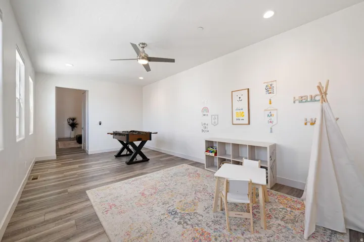 Spacious room featuring wood-finish flooring, recessed lighting, a modern ceiling fan, and multiple windows