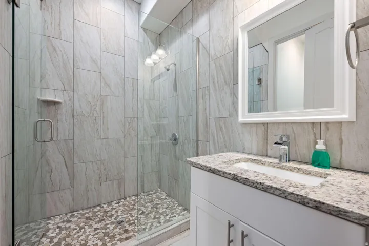 Contemporary bathroom featuring a frameless glass shower enclosure with pebble floor tiles and large format wall tiles