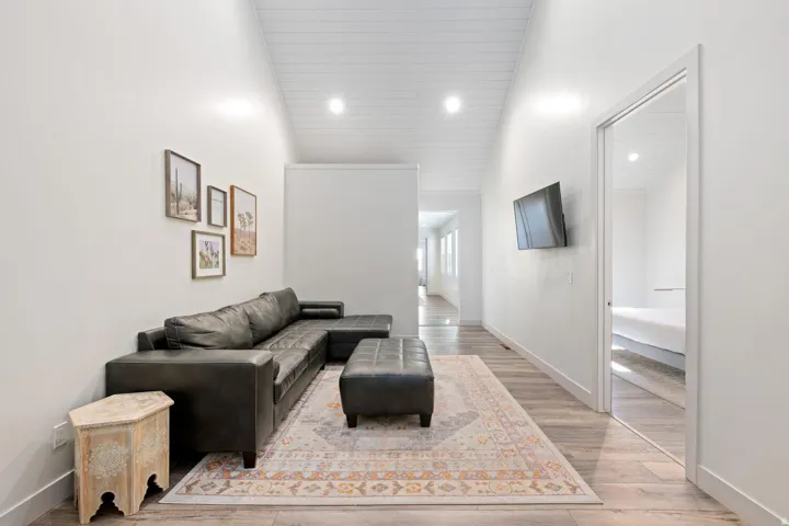 Spacious area featuring wood-finish flooring, white walls, and a vaulted ceiling with recessed lighting