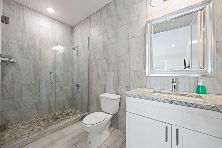 Glass-enclosed shower with pebble flooring and tiled walls