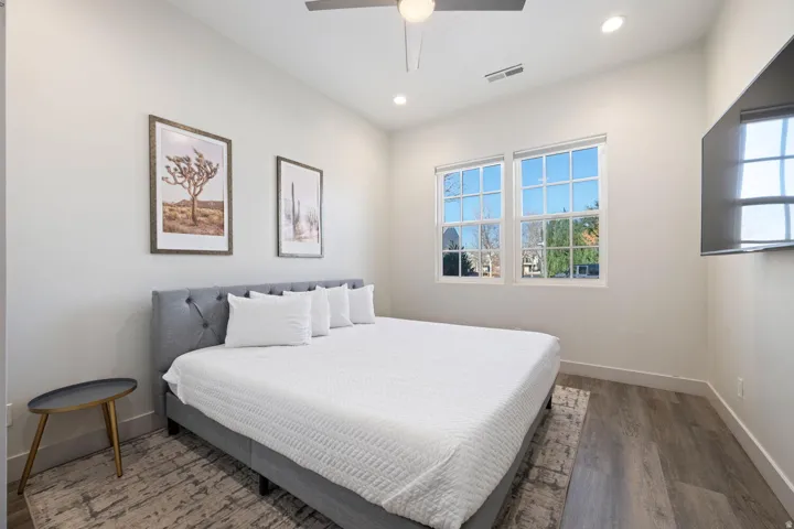 Room featuring wood-finish flooring, two large windows, a ceiling fan with integrated lighting, recessed lighting, and a wall-mounted television