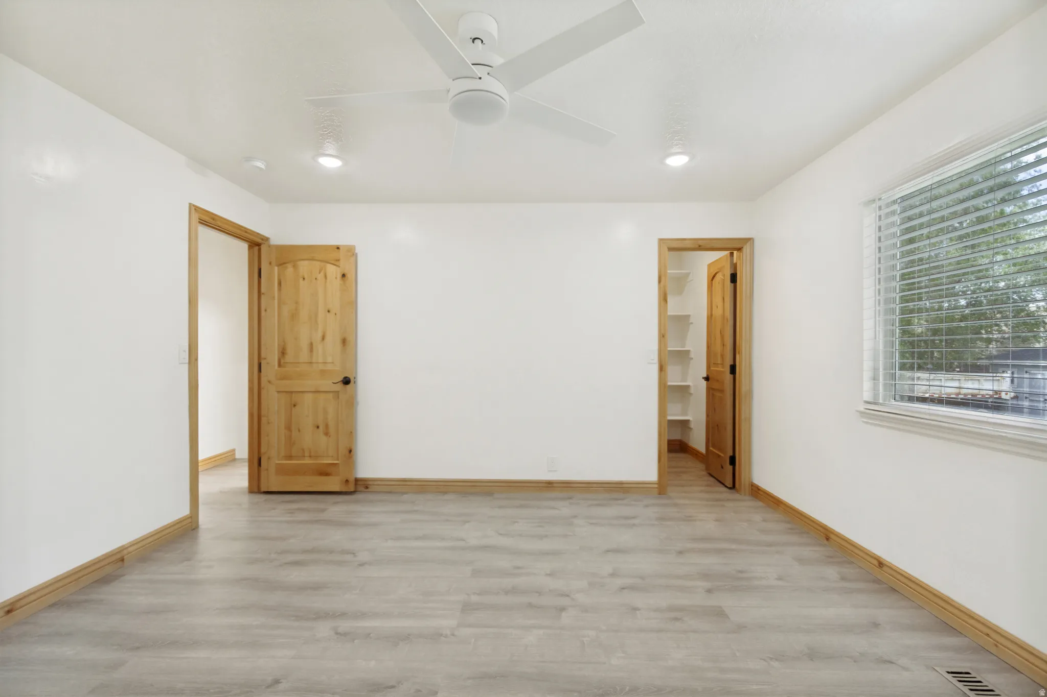 Spacious interior room featuring light wood-finish flooring, white walls, and natural wood trim