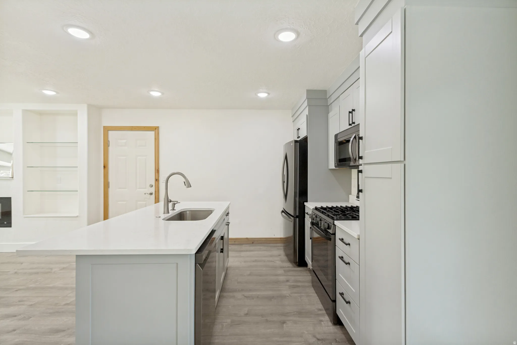 Contemporary kitchen featuring light-toned cabinetry, stainless steel appliances, a center island with an undermount sink, and recessed lighting