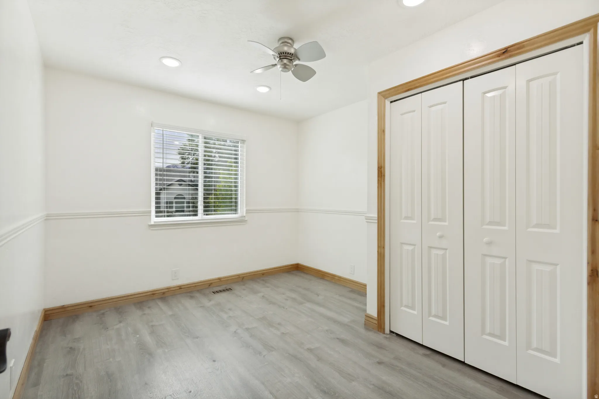 Room featuring light wood-finish flooring, white walls with chair rail molding, and a window with blinds