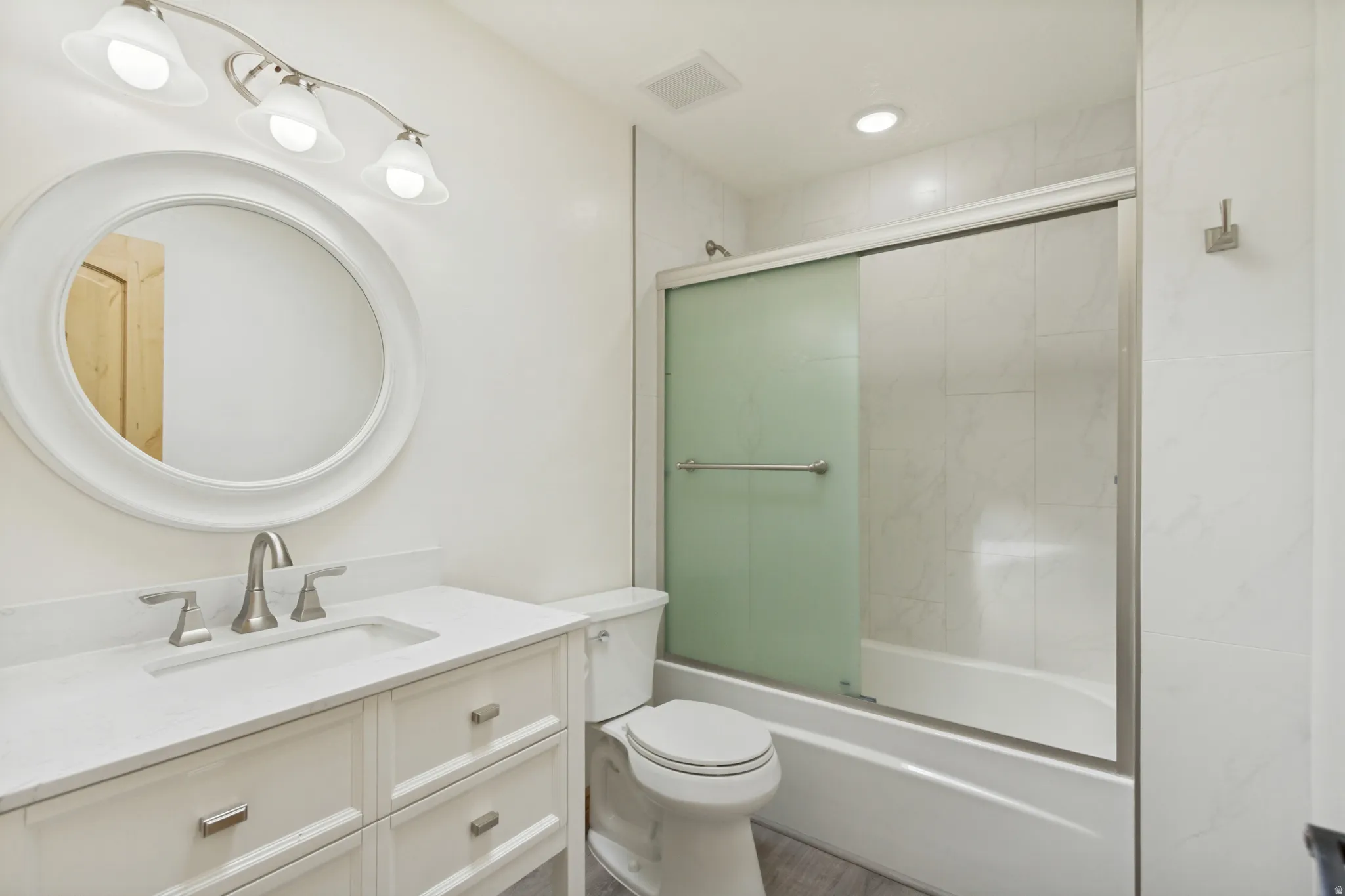 Bathroom featuring a white vanity with an integrated sink, brushed nickel fixtures, and a circular framed mirror
