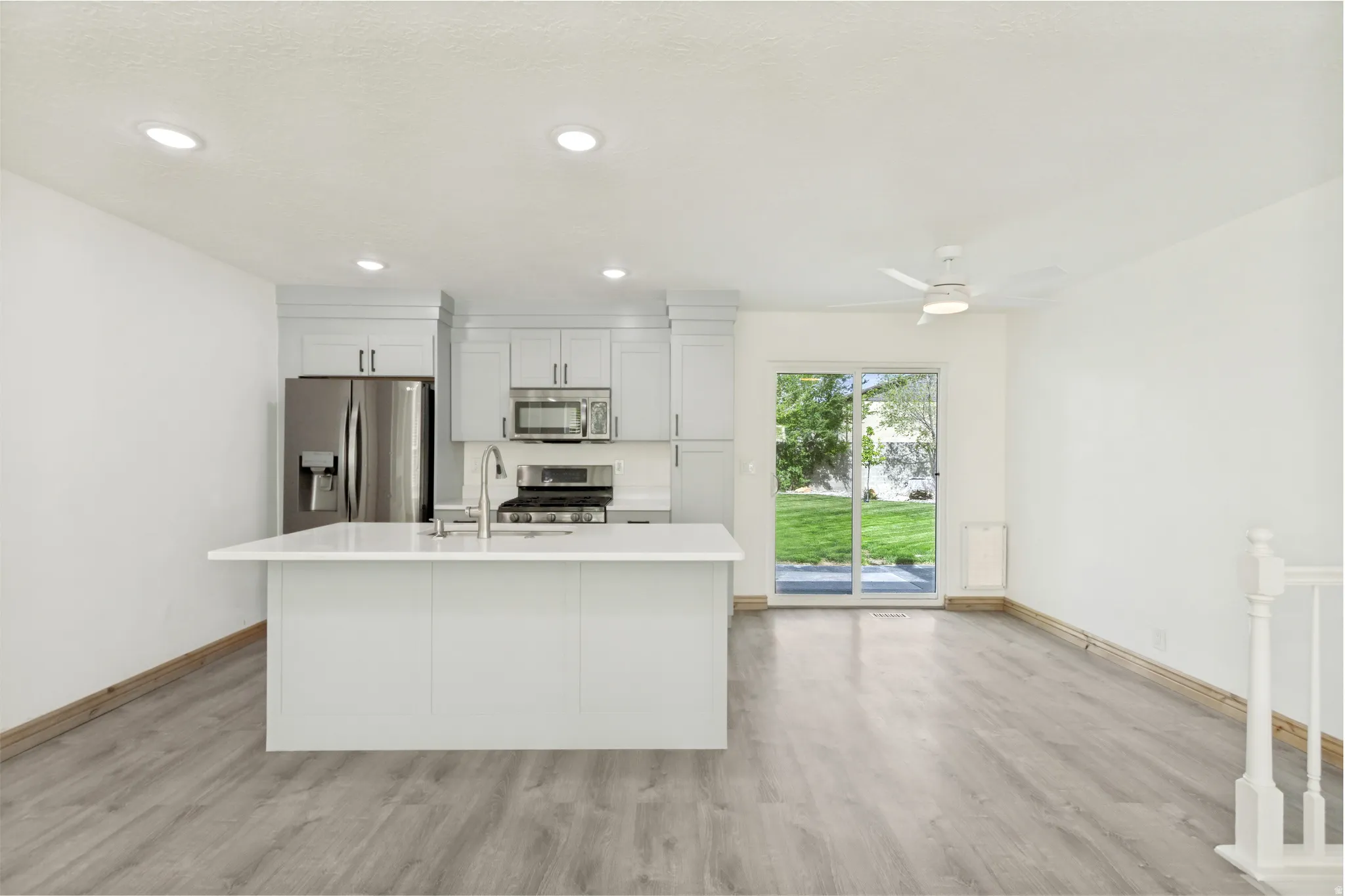 Modern kitchen featuring a central island with a sink, stainless steel appliances, light-toned cabinetry, and recessed lighting