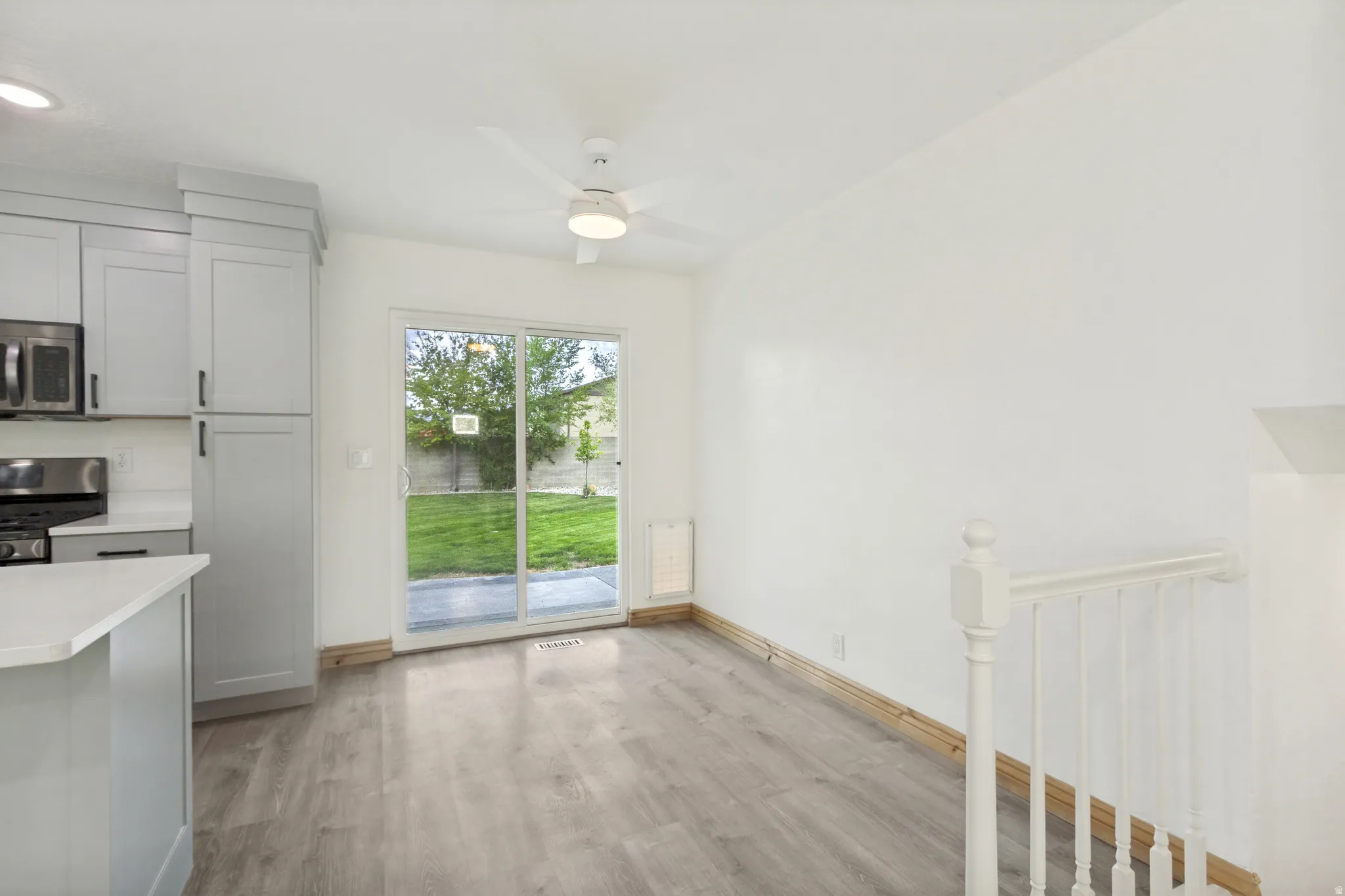 Open-concept kitchen and dining area featuring light wood-finish flooring, a contemporary ceiling fan, and a sliding glass door providing direct access to the outdoor space