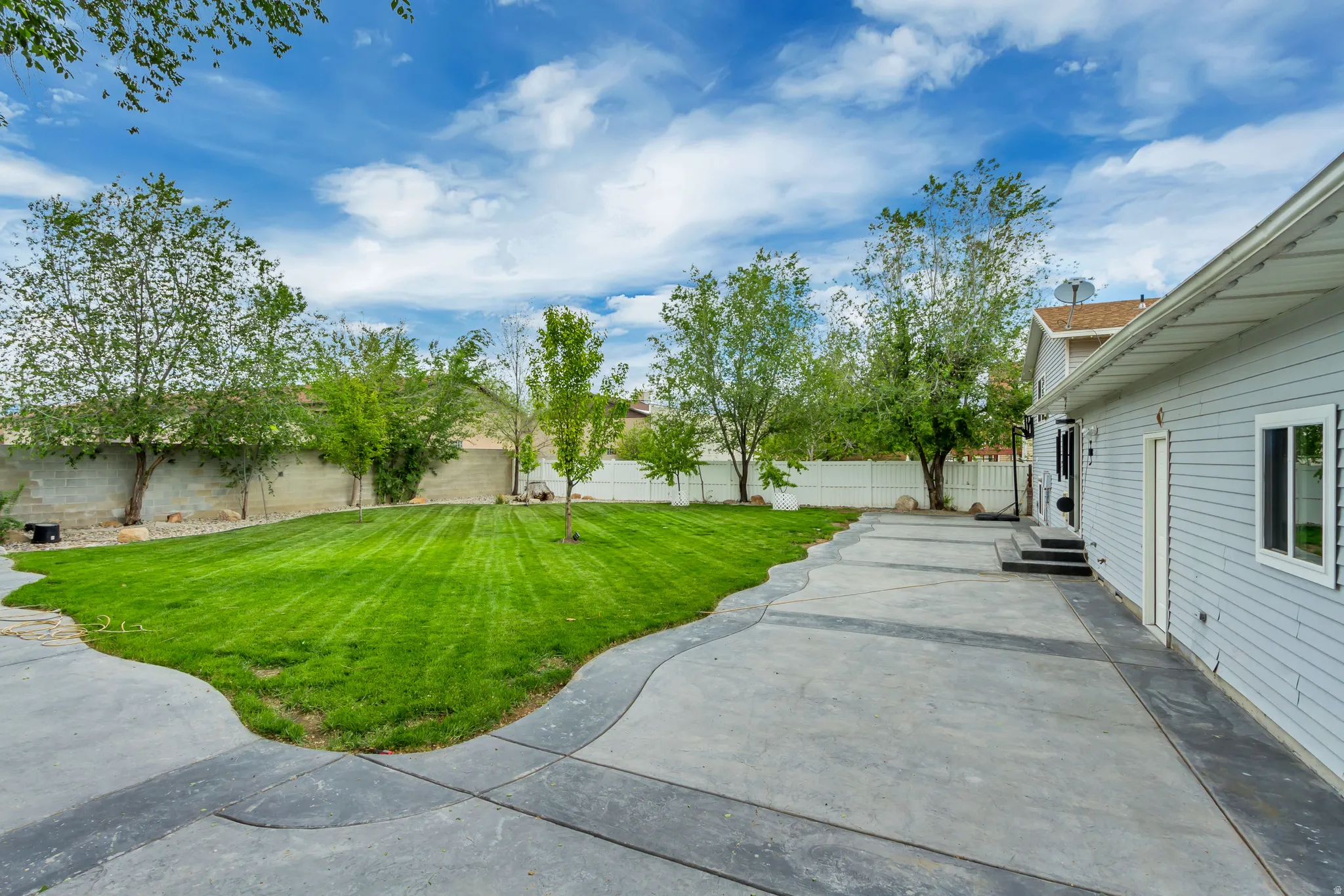 Expansive backyard featuring a lush lawn, mature trees, and a patterned concrete patio