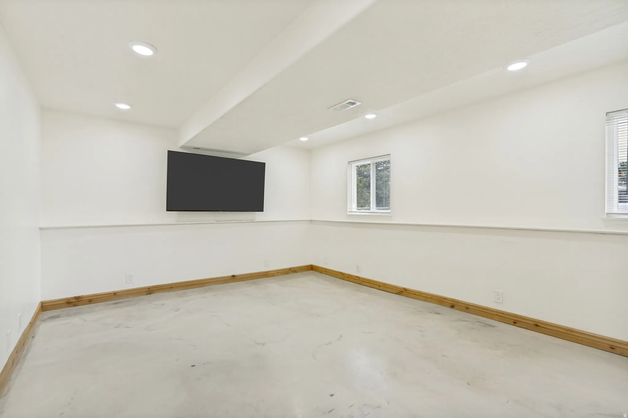 Spacious room featuring light-toned flooring, recessed ceiling lighting, and a mounted screen