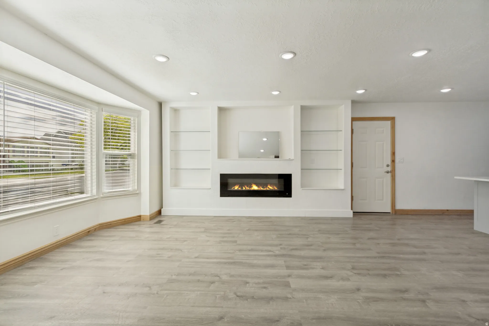 Spacious interior featuring wood-finish flooring, a contemporary built-in electric fireplace, recessed lighting, and a bay window