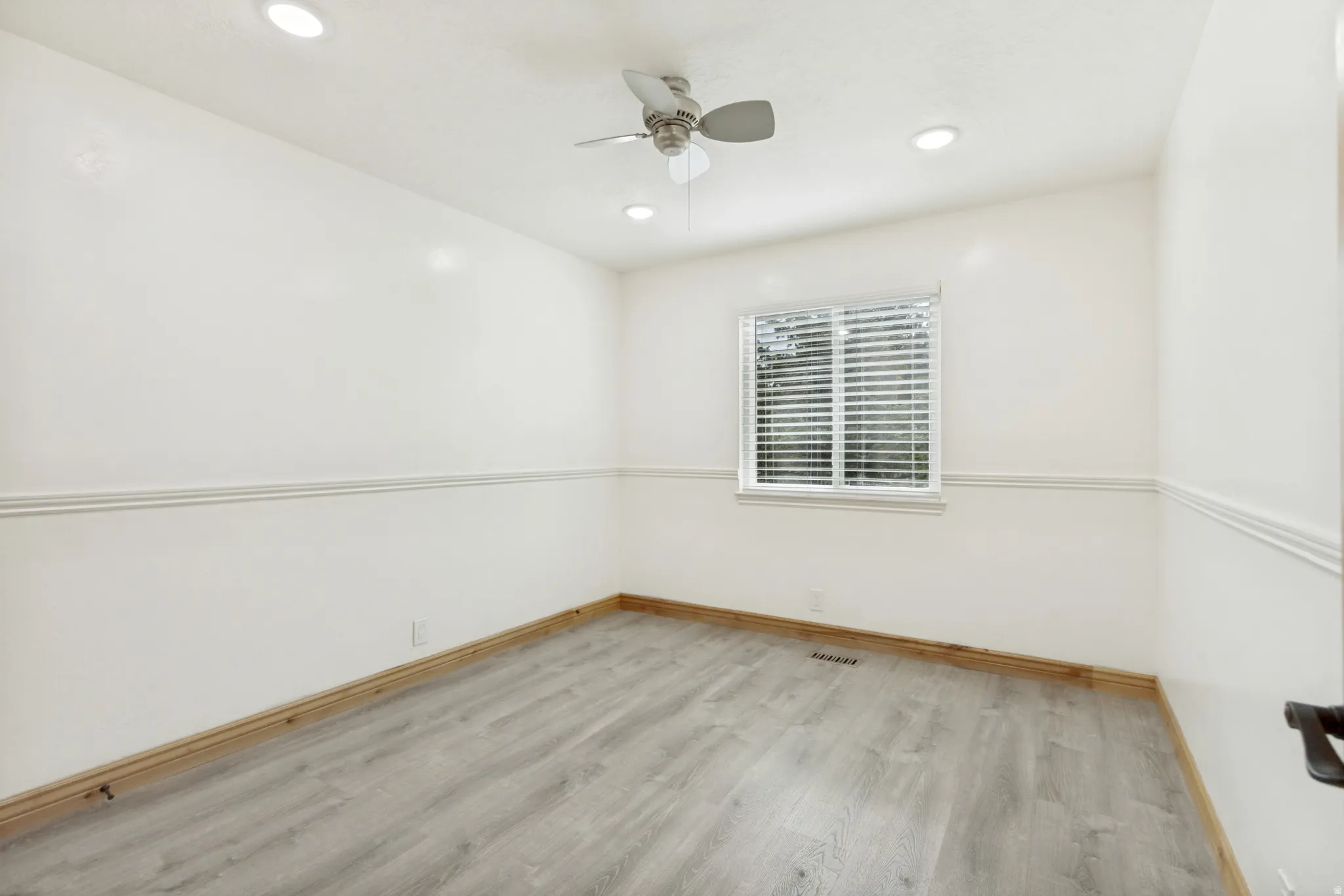 Room featuring light wood-finish flooring, white walls with chair rail molding, and a window with blinds