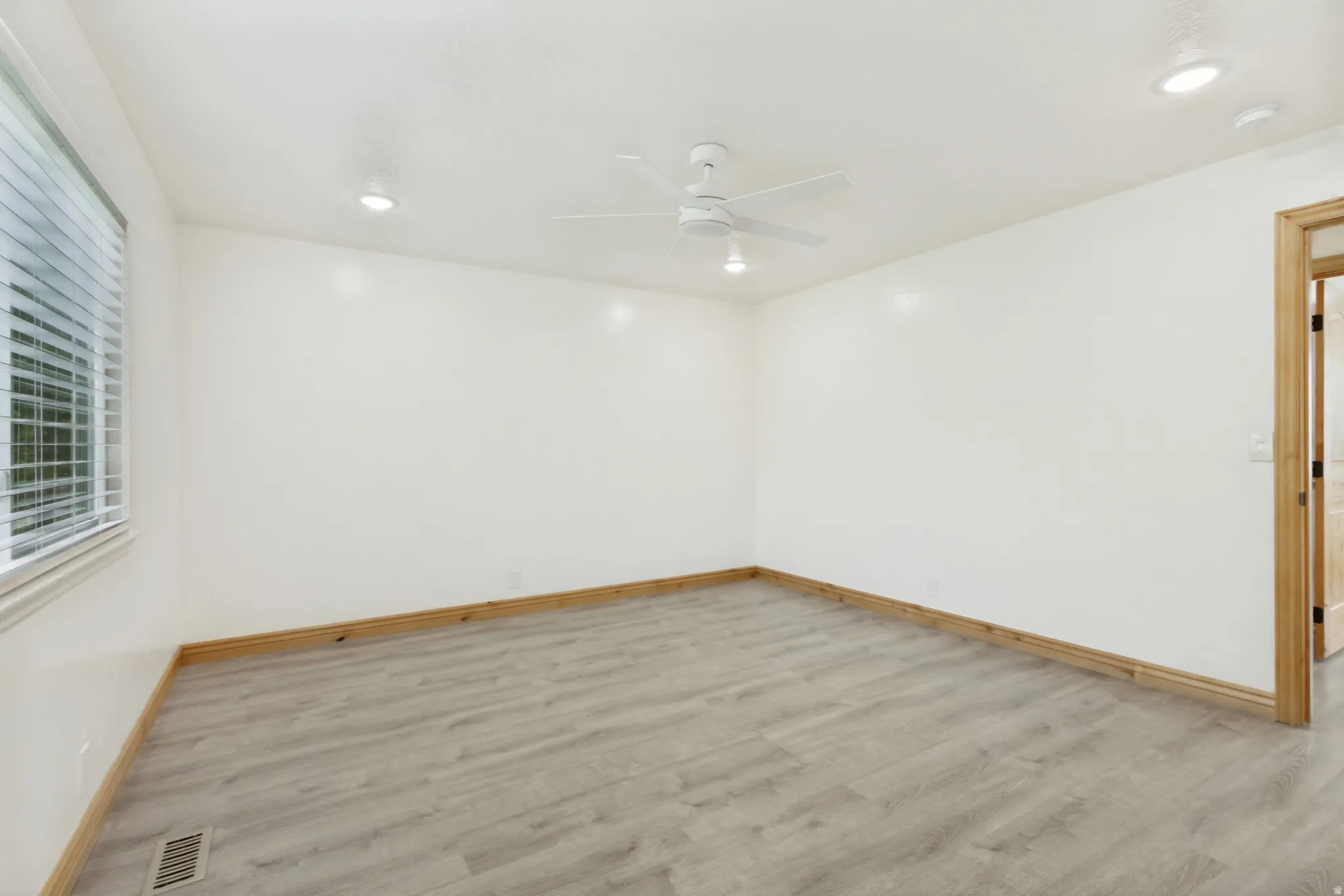 Spacious room featuring wood-finish flooring, a ceiling fan with integrated lighting, recessed ceiling lights, and a window with blinds