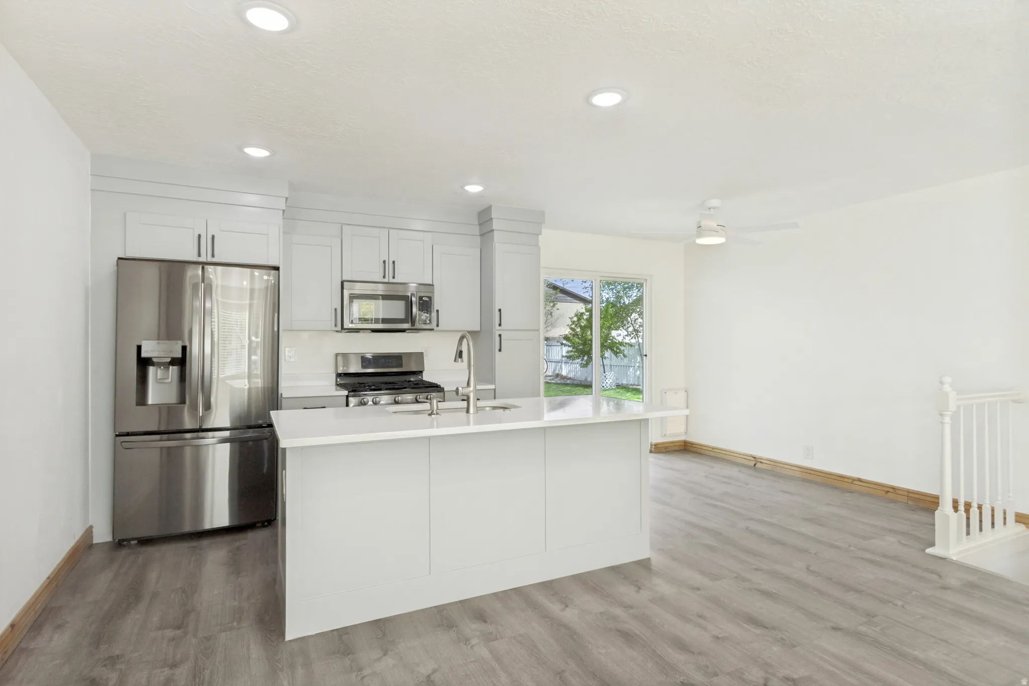Modern kitchen featuring light gray shaker cabinets, white subway tile backsplash, stainless steel appliances, and an island with a white countertop