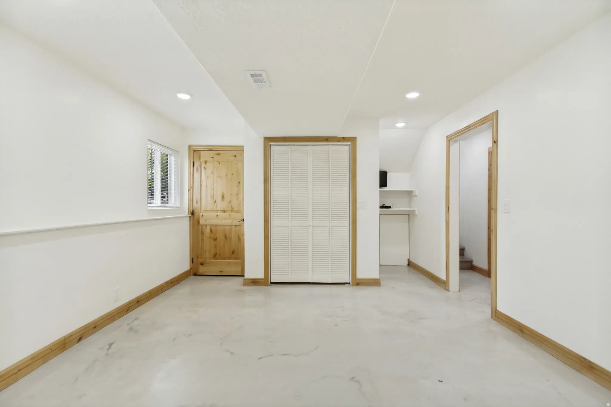 Open concept room featuring a light-toned concrete floor, recessed lighting, and white walls with natural wood trim