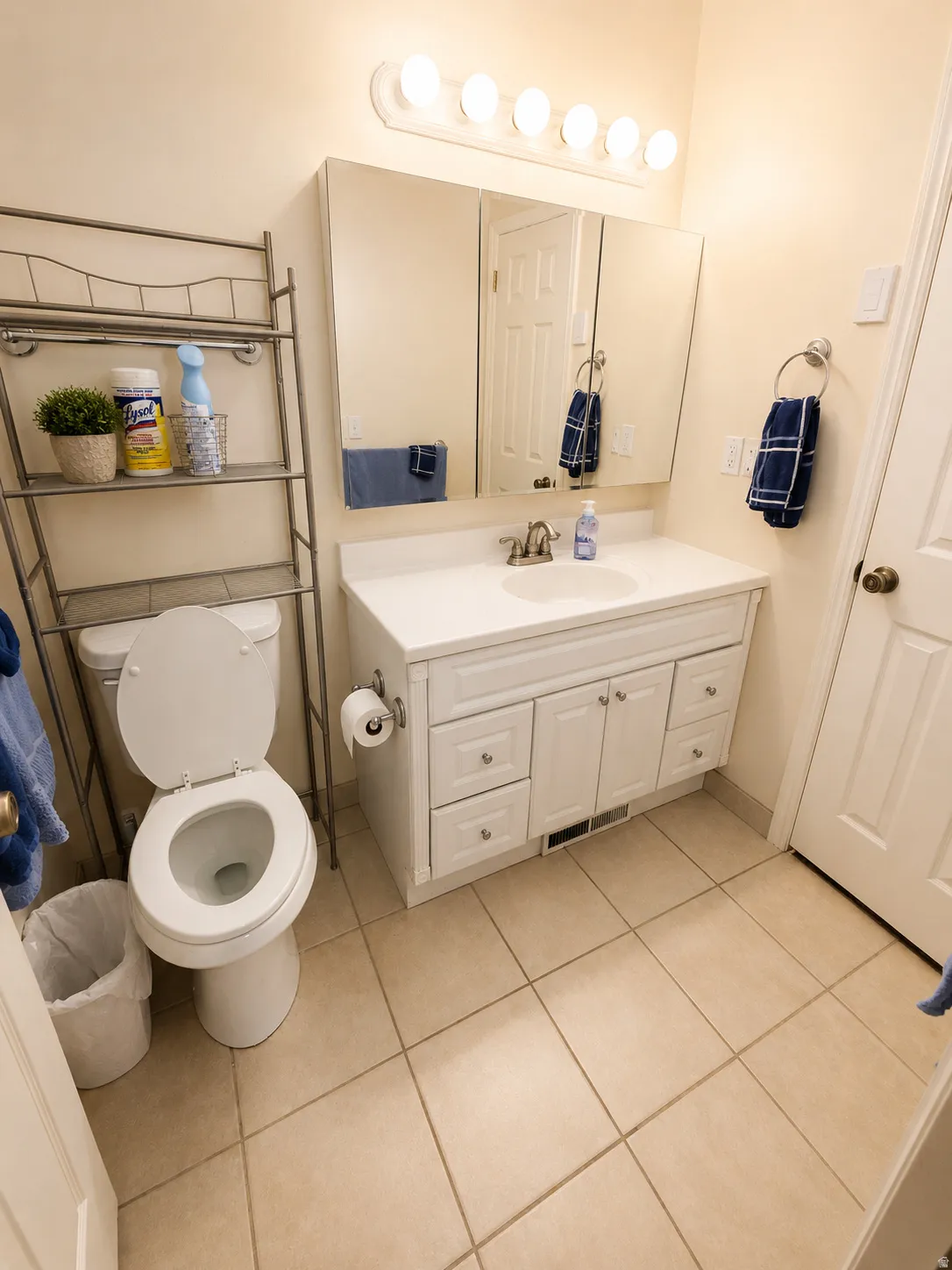Bathroom featuring a white vanity with integrated sink, a three-panel mirrored medicine cabinet, a wall-mounted light fixture with five bulbs, neutral-toned floor tiling, and a white toilet, Walk In Shower.