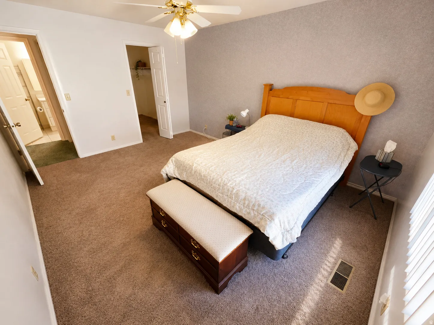 Carpeted room featuring a ceiling fan with integrated lighting, textured wall finish, and an entryway to another room with a visible white toilet and vanity