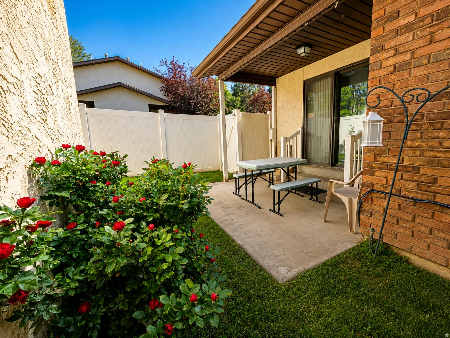 Private outdoor patio featuring a concrete surface, mature red rose bushes, a small grass area, and a privacy fence