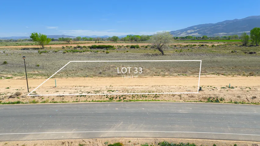 Expansive vacant lot featuring a clear building area, paved road frontage, and distant mountain scenery