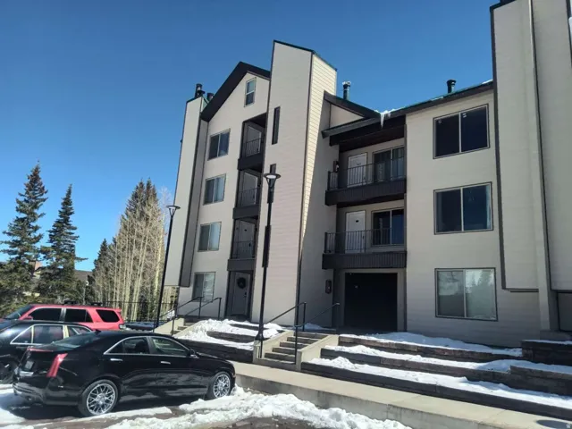 Modern multi-story building featuring multiple balconies, exterior lighting, and a paved parking area