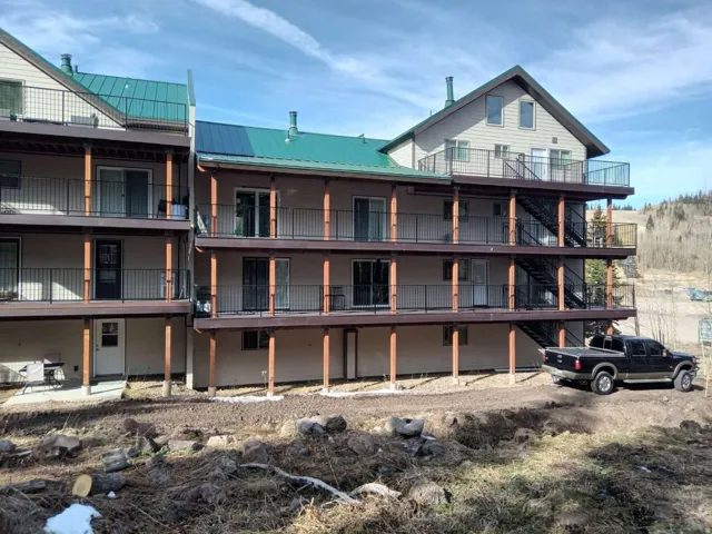 Multi-level building exterior featuring multiple balconies, a green metal roof, and light-colored siding