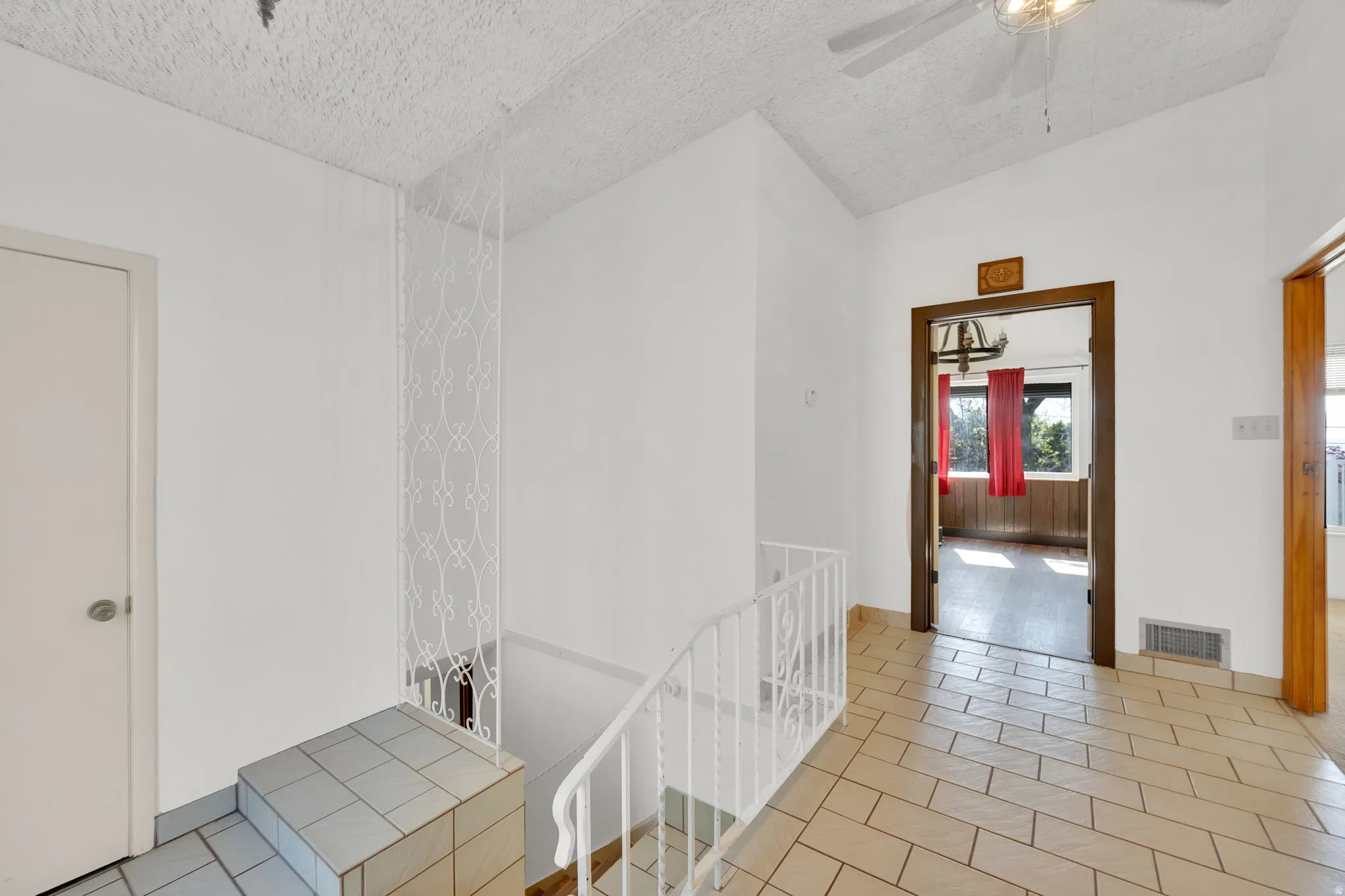 Hallway featuring light-toned tile flooring, white walls, and a textured ceiling