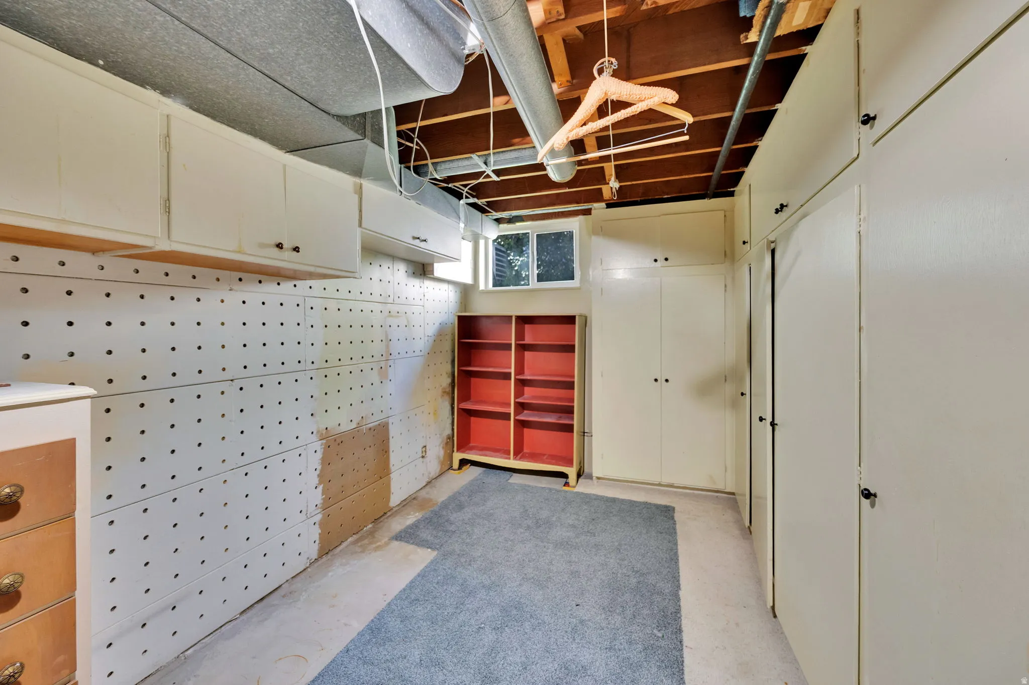Utility room featuring extensive built-in cabinetry, pegboard wall panels, exposed ceiling joists, and a window for natural light