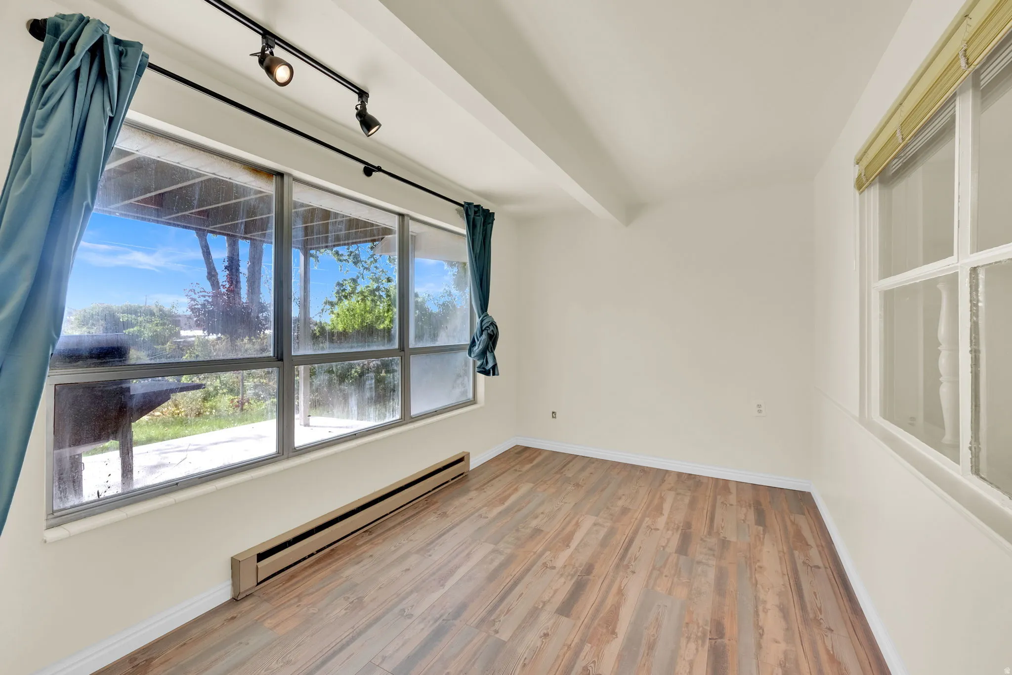 Bright room featuring wood-finish flooring, a large multi-pane window, track lighting, and baseboard heating