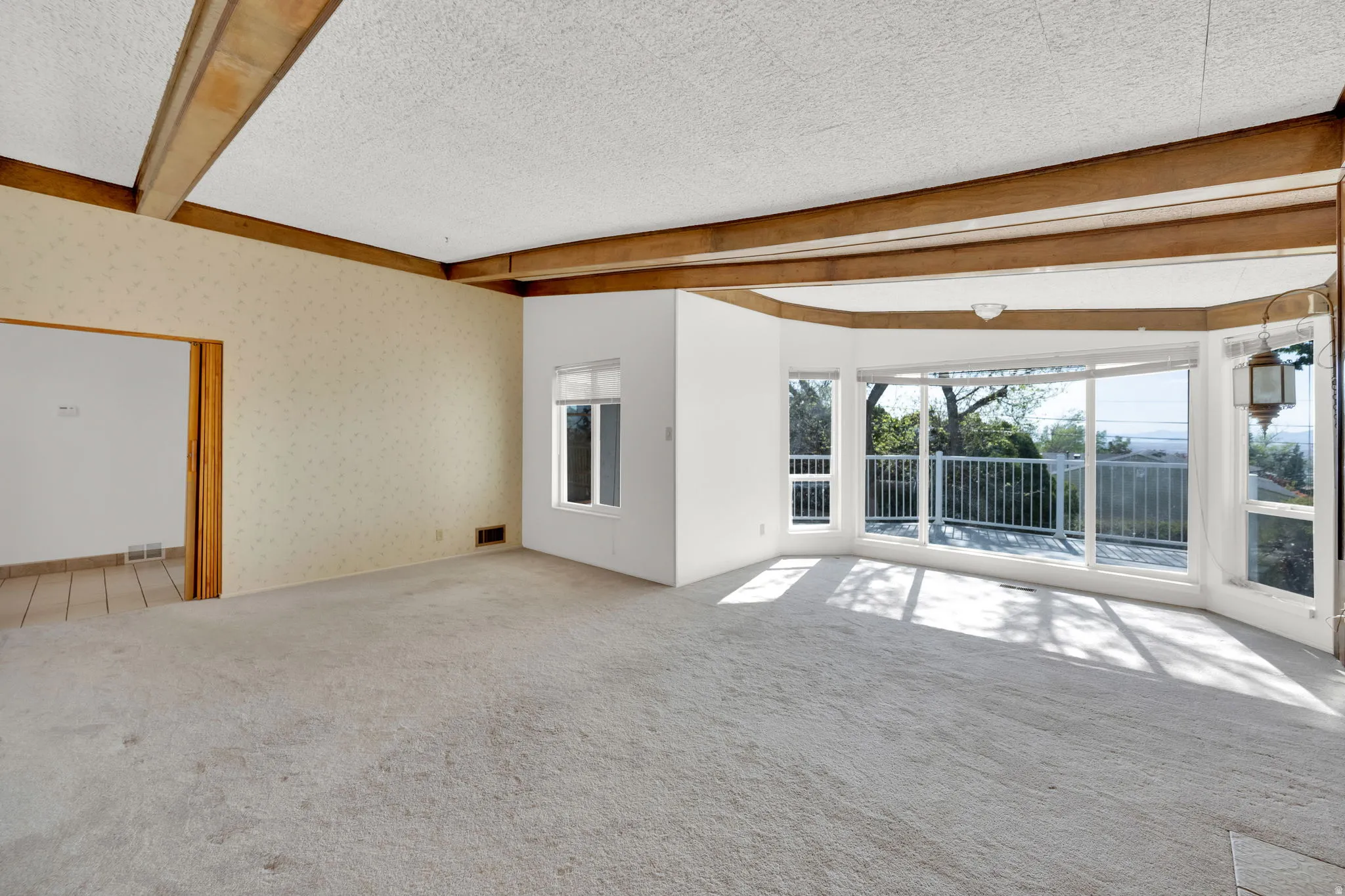 Spacious room featuring exposed wood beams, expansive floor-to-ceiling windows, and light-colored carpeting