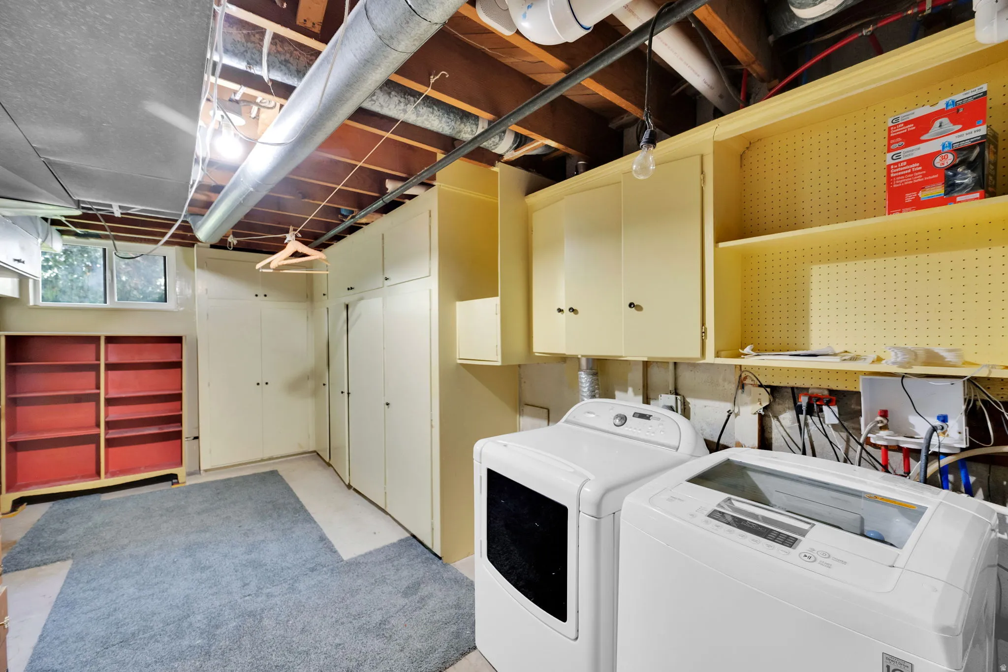Laundry area featuring a window, overhead cabinetry, pegboard shelving, built-in storage closets, and exposed ceiling beams