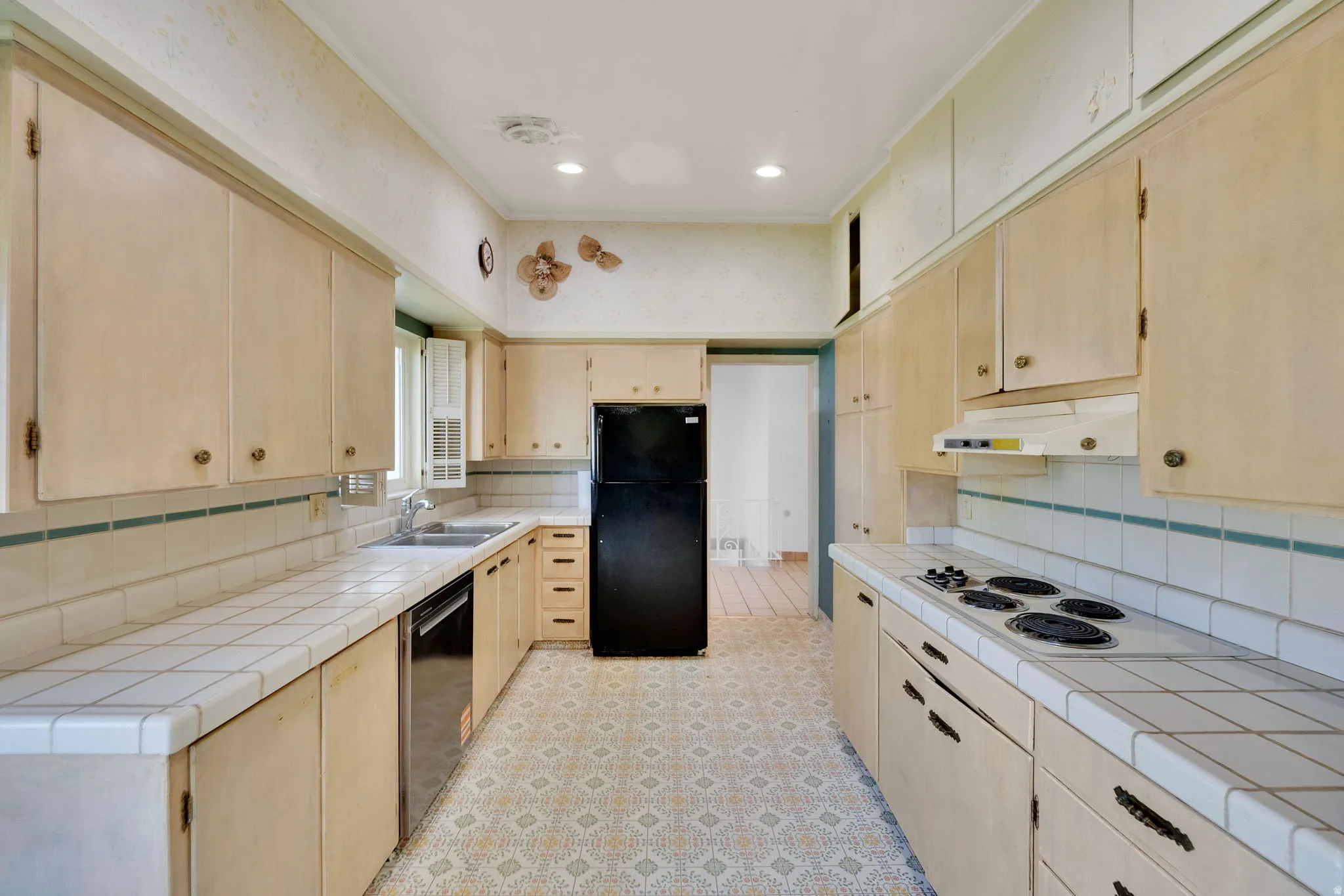 Galley kitchen featuring extensive upper and lower cabinetry, white tile countertops, and patterned floor tile