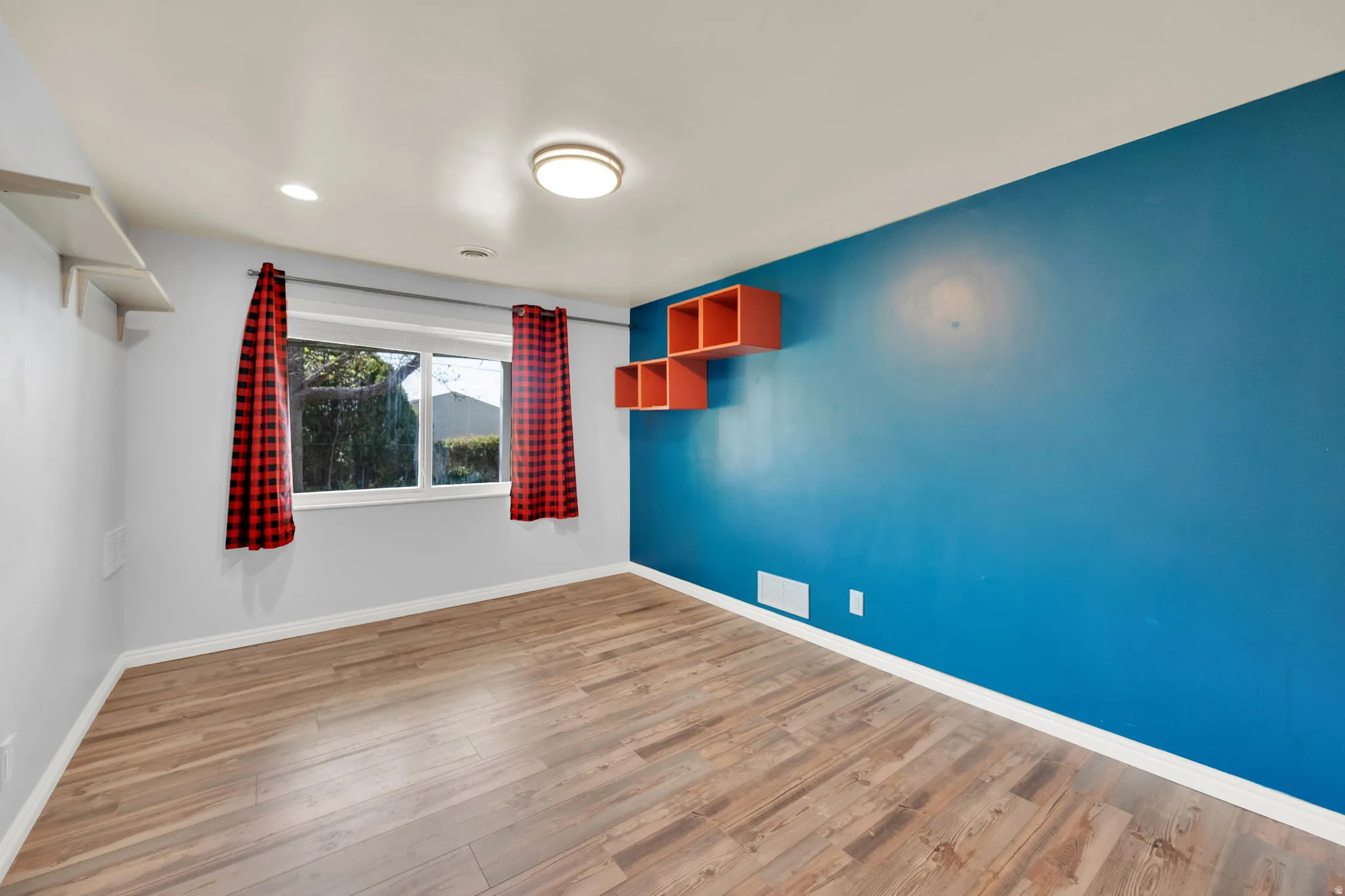 Room featuring wood-finish flooring, a prominent accent wall, and built-in floating shelves
