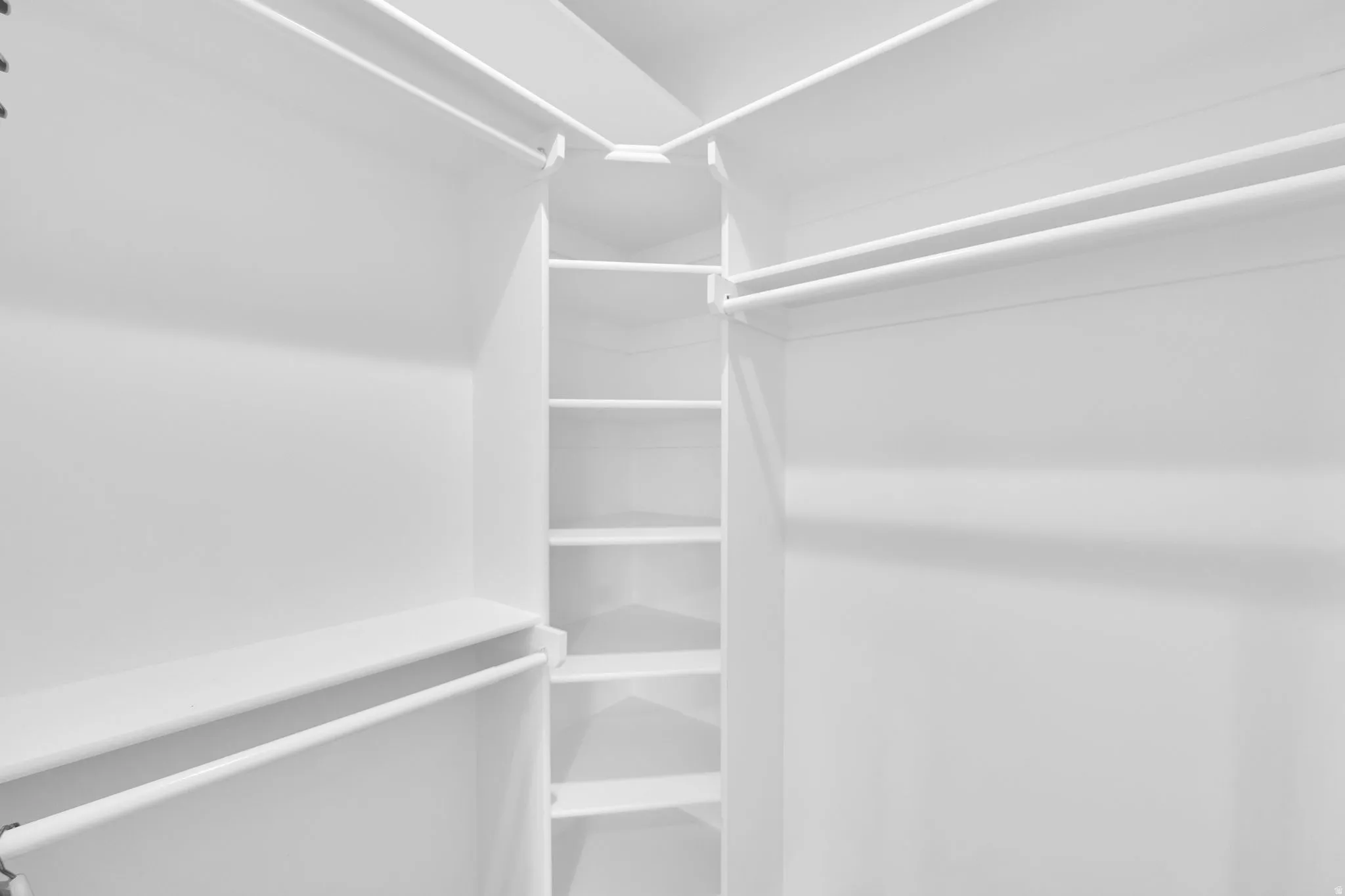 Spacious walk-in closet featuring white built-in shelving, multiple hanging rods, and ample storage capacity